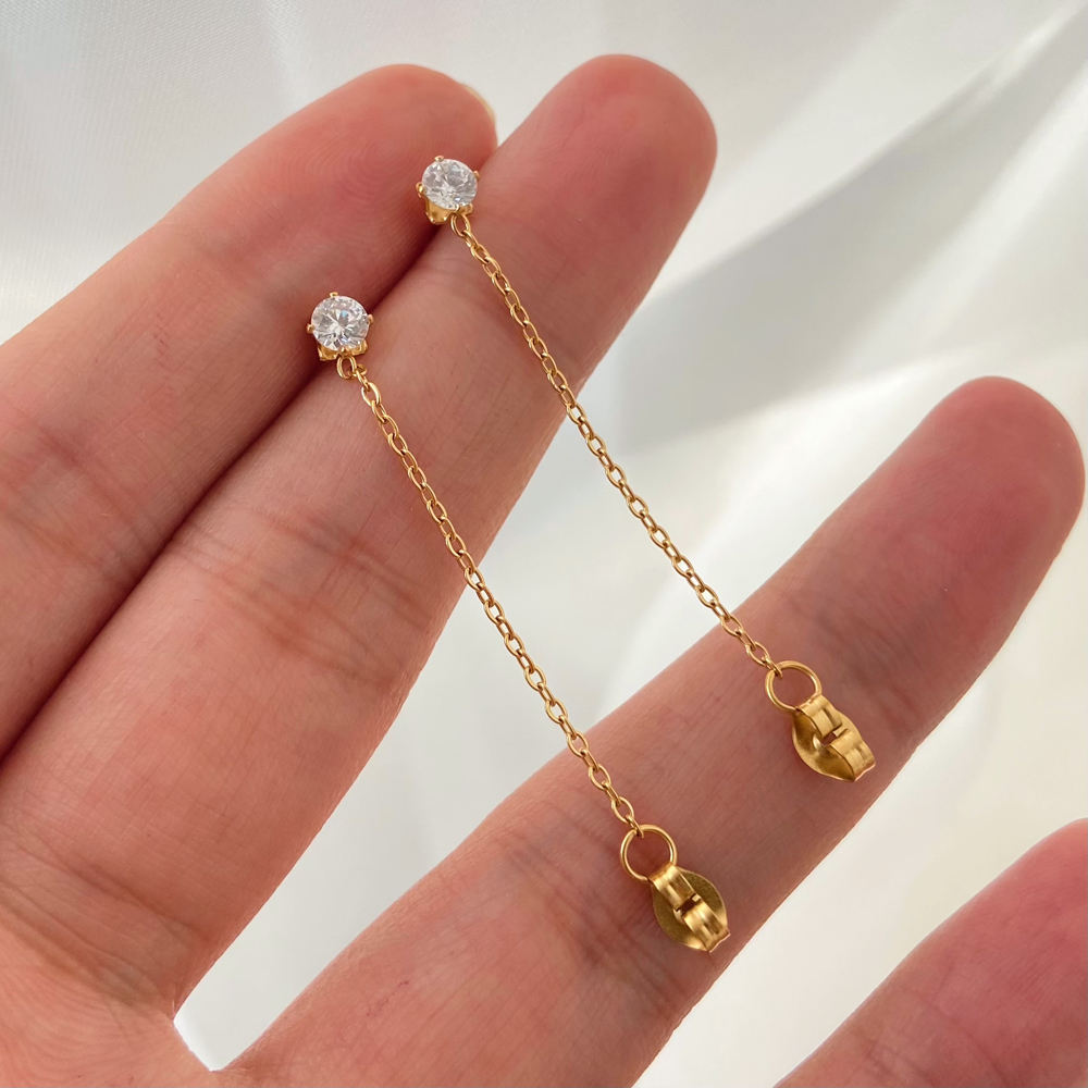 Gold chain earring with clear gemstones held between fingers against a neutral background