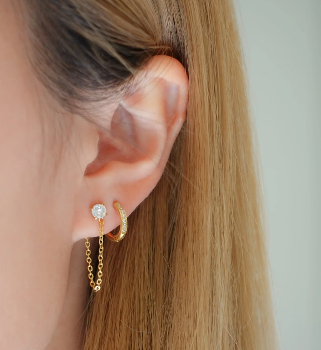Close-up of an ear wearing gold hoop earrings with a blurred background