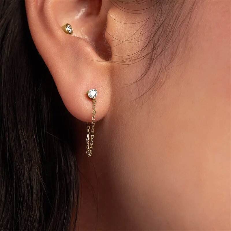 Close-up of an ear with a gold earring featuring a small diamond and a chain detail.