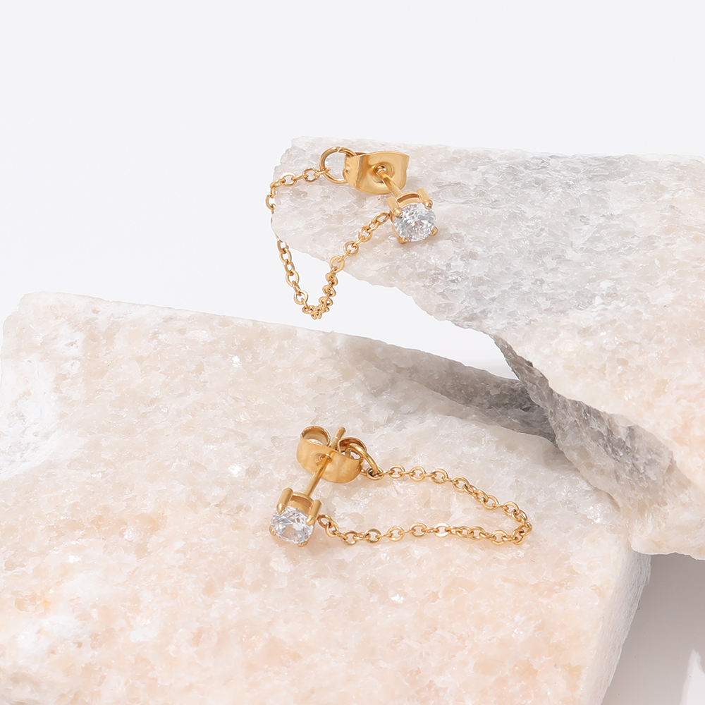 Gold chain earrings with clear gemstones on a light stone surface