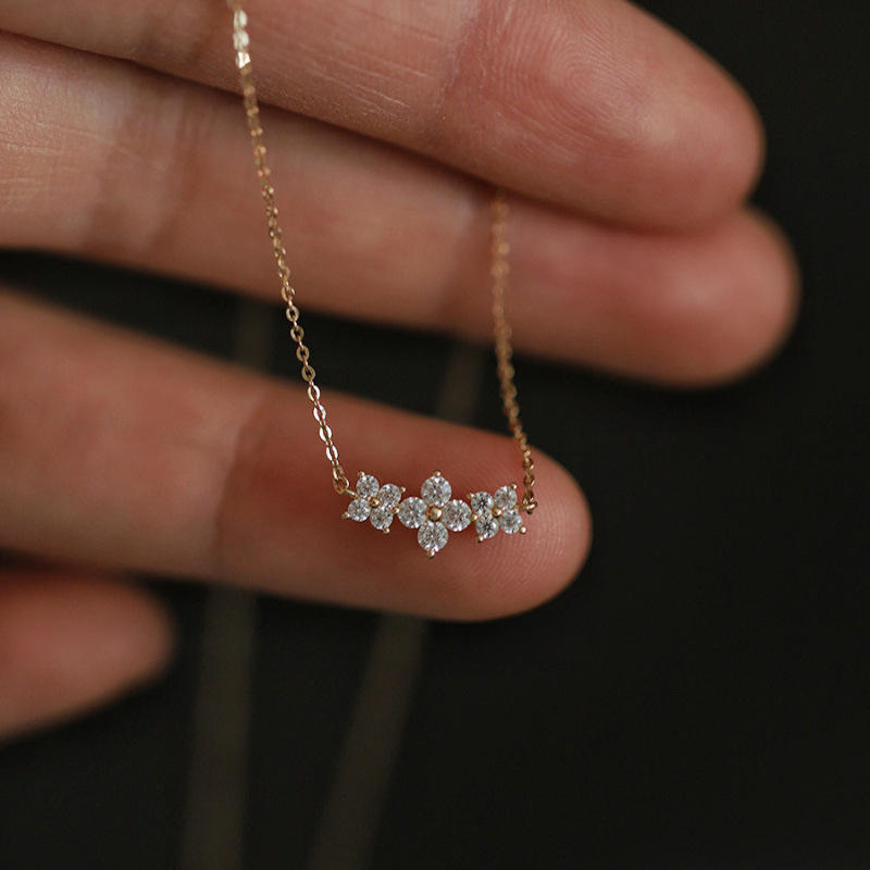Delicate diamond necklace held between fingers against a dark background