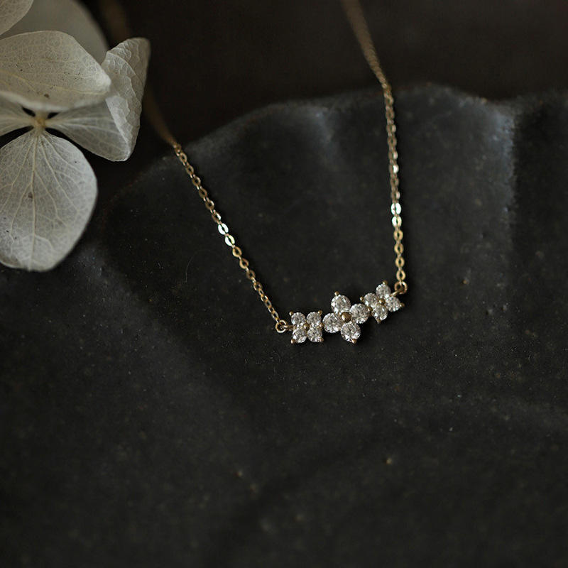 Gold necklace with diamond-like stones on a dark surface with a white leaf.