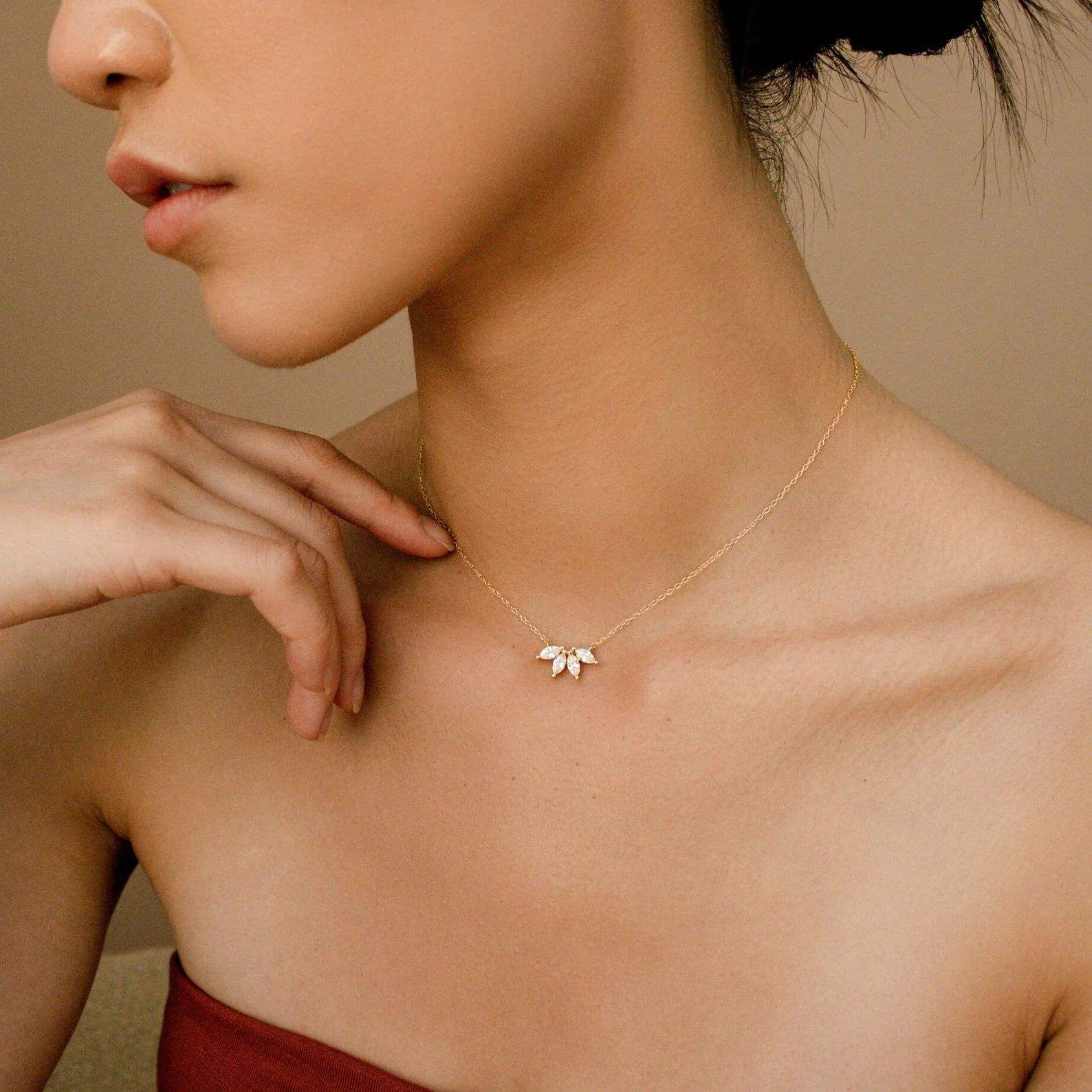 Woman wearing a delicate gold necklace with a leaf pendant against a neutral background