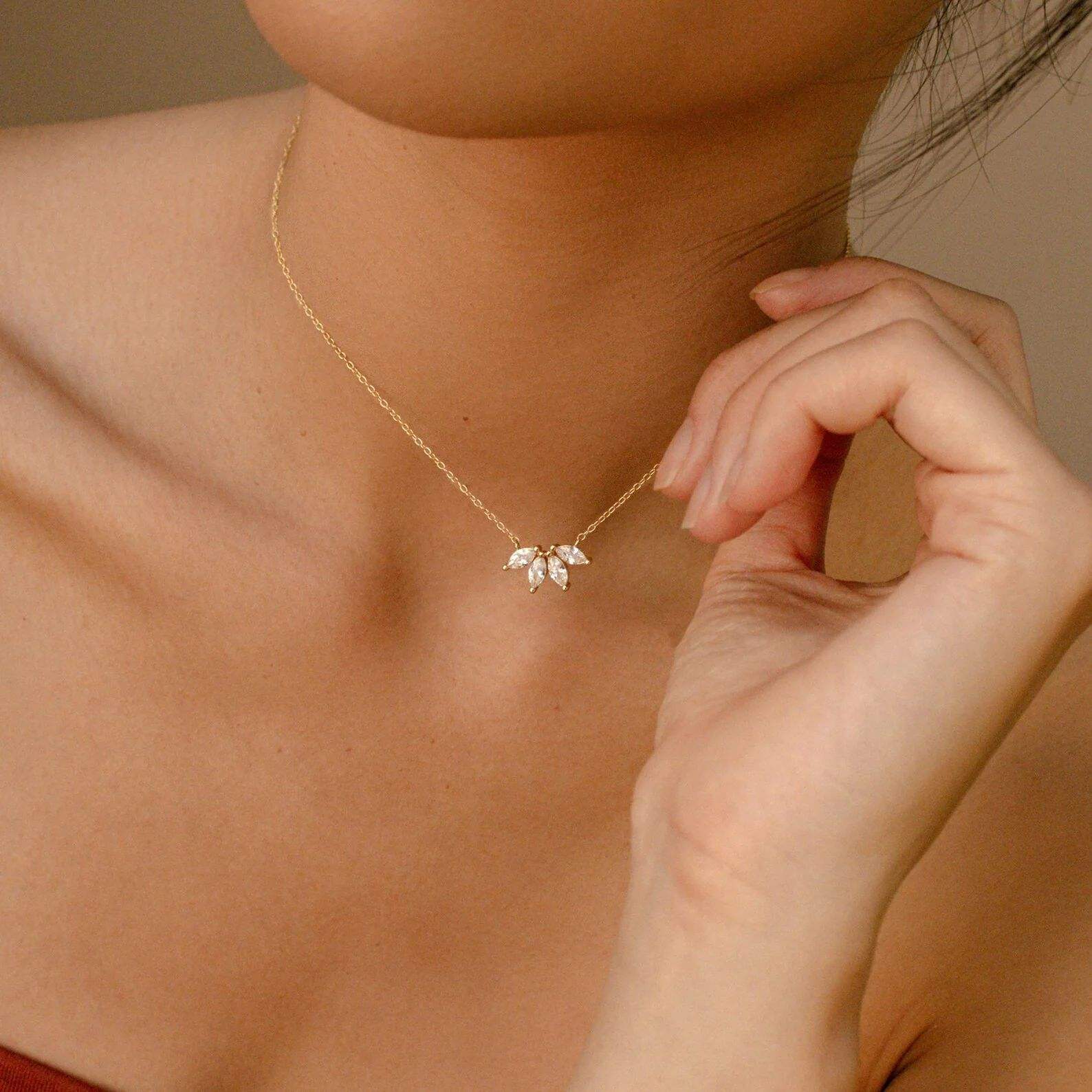Gold necklace with a leaf-shaped pendant worn by a person against a neutral background