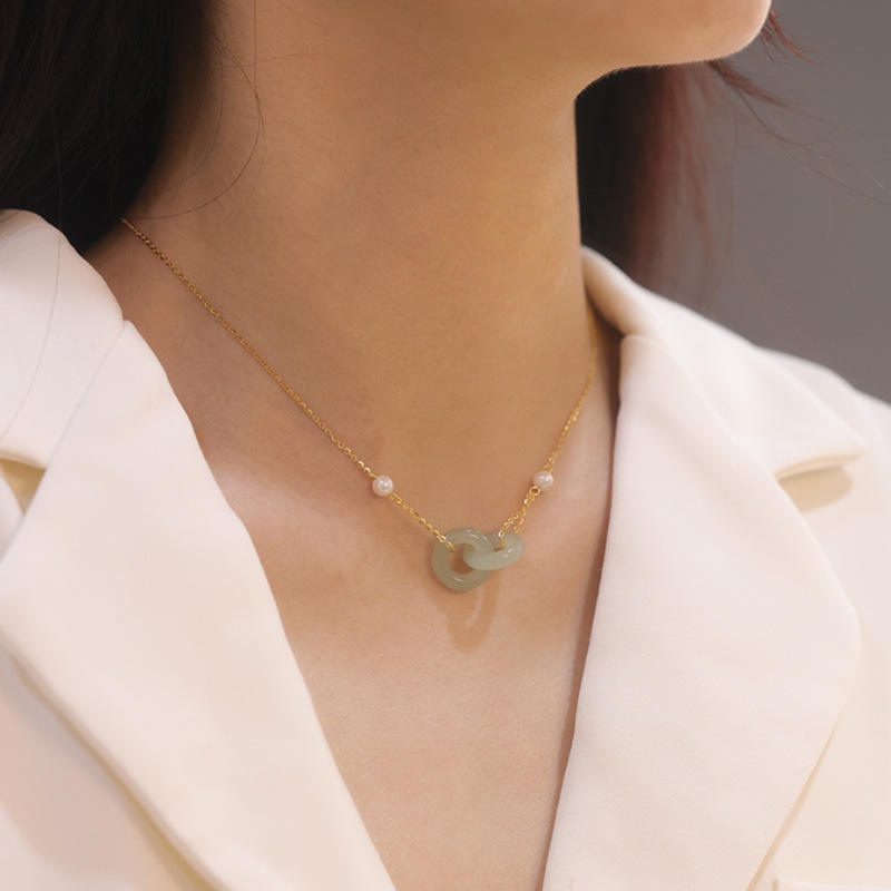 Necklace with a green pendant worn by a person in a white blazer.