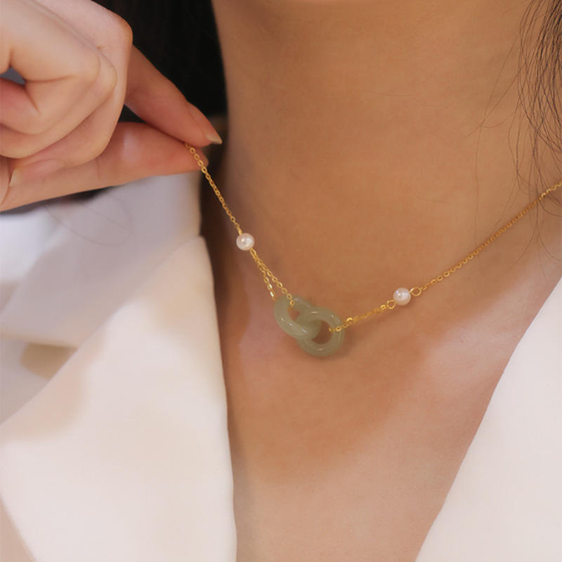 Necklace with green jade pendant and pearls being adjusted on a person wearing a white outfit.
