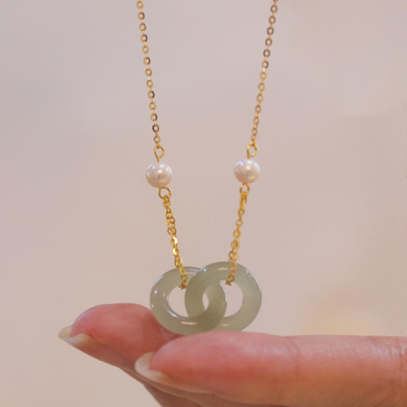 Necklace with a jade pendant and pearls held by a hand against a neutral background