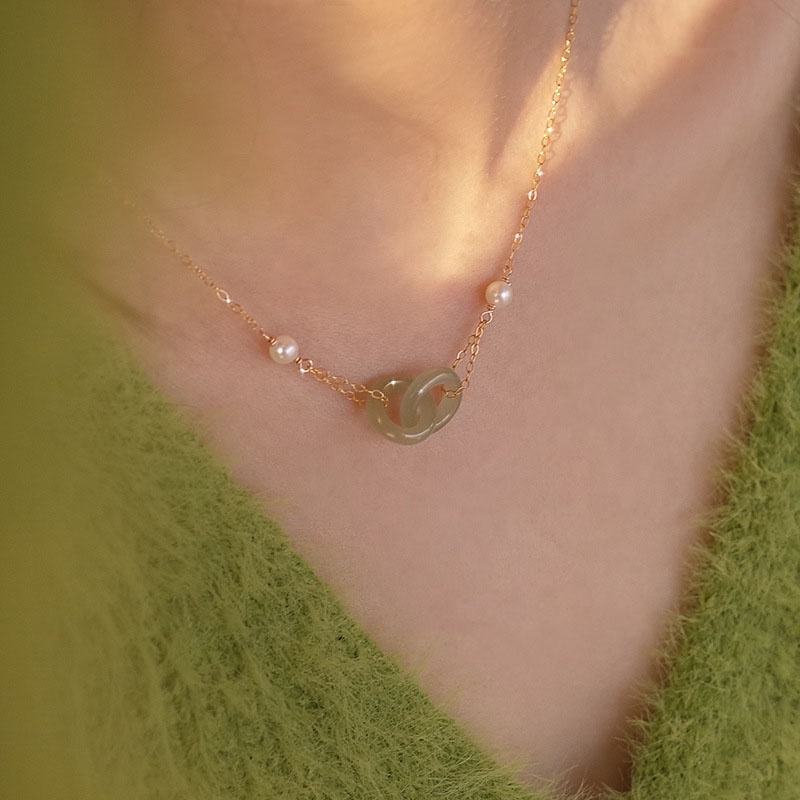 Gold necklace with a green pendant worn by a person against a green background